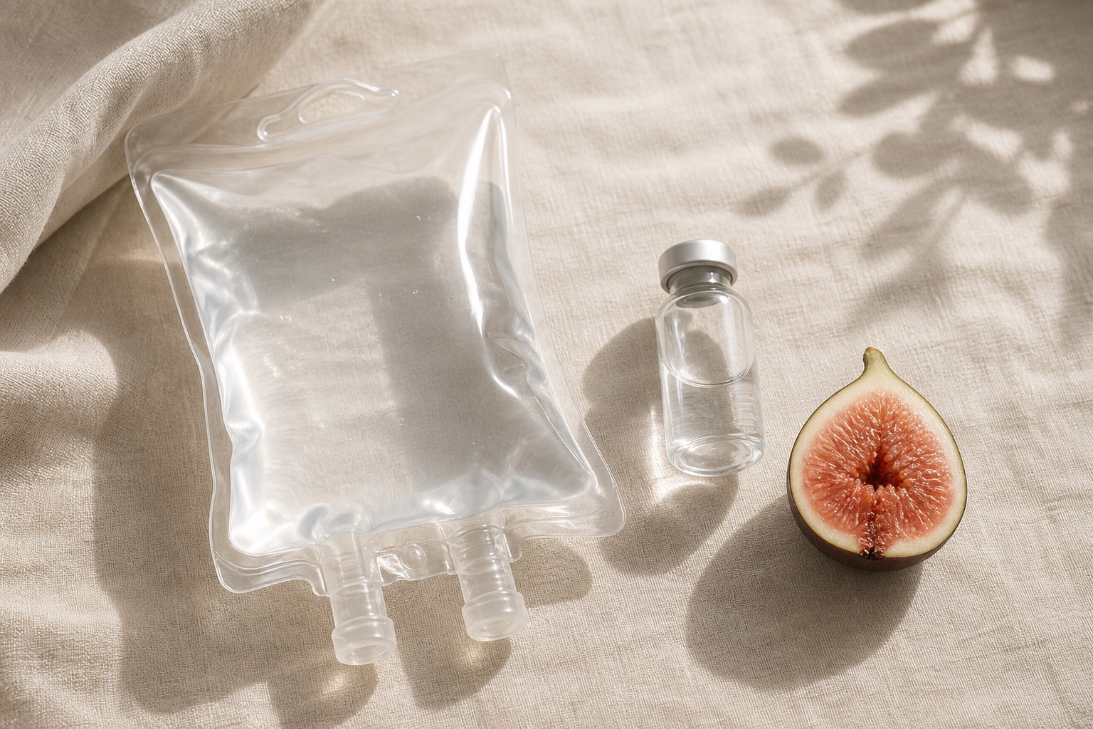 A glowing still life with an IV bag, serum vial, and halved fig on linen.