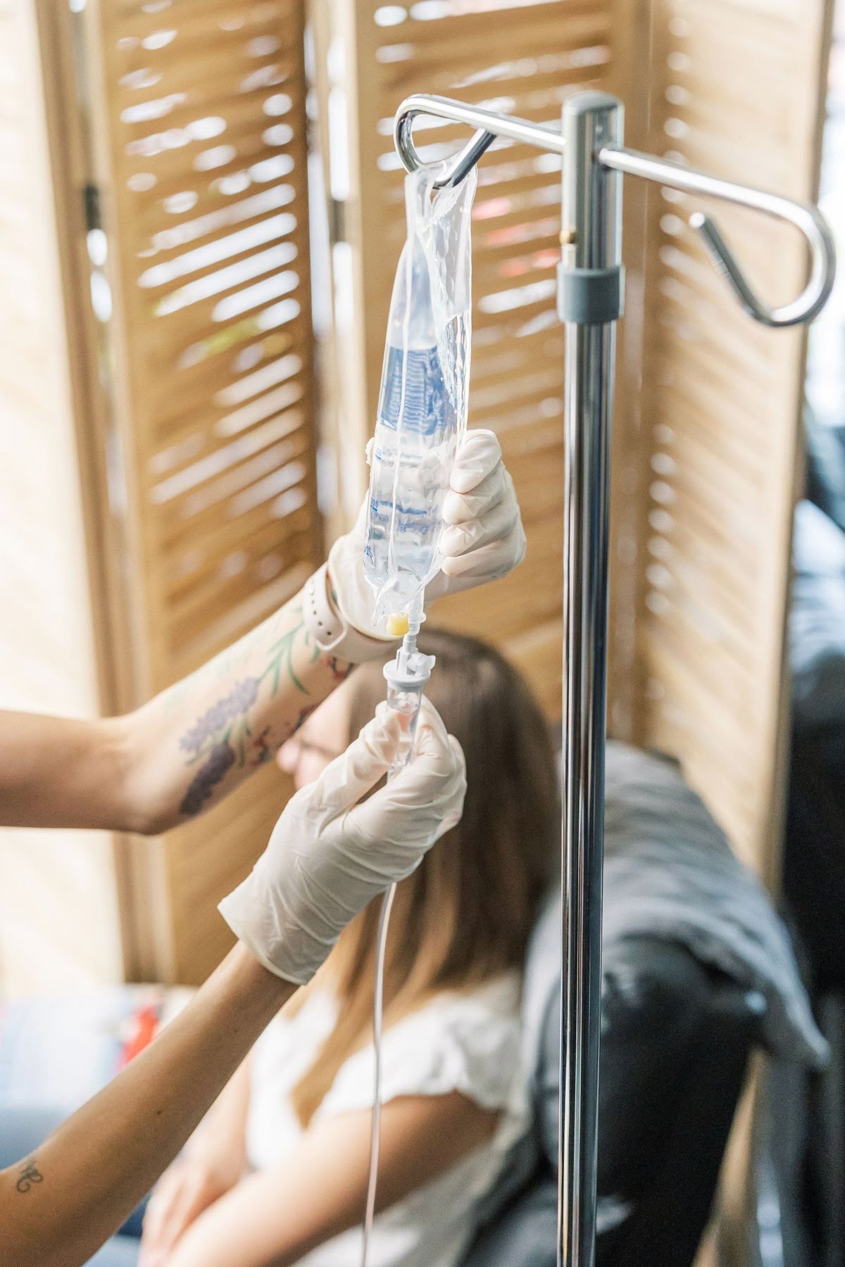 A nurse's gloved hands setting up an IV bag and tubing for a client.